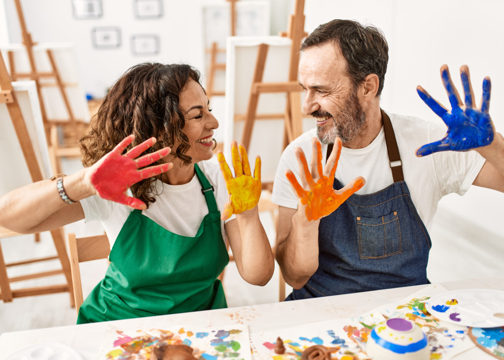 Two adults joyfully showing their paint-covered hands in an disability day programs art therapy class.
