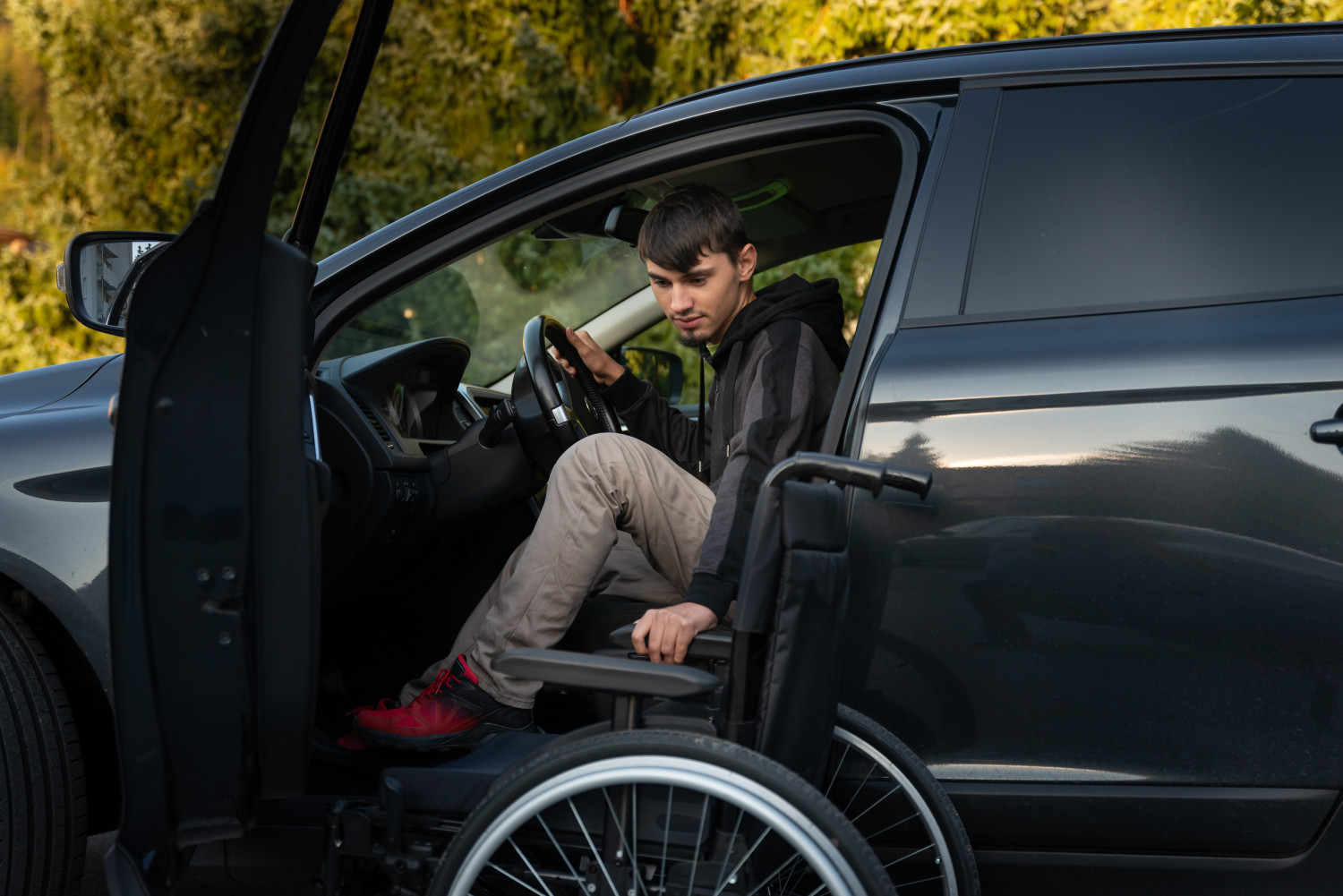 A man is transitioning from a manual wheelchair into the driver's seat of a black car, showcasing the vehicle modifications available to those from the NDIS disability transport services