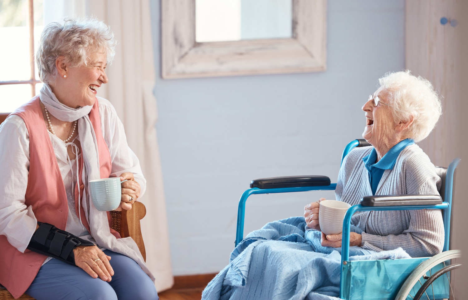 Two senior individuals sharing a laugh over a cup of tea in a respite care setting, showing the social opportunities available in respite care environments.
