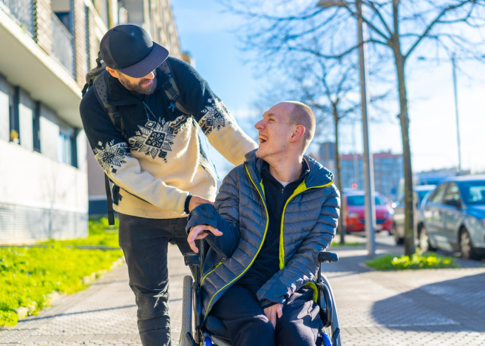 Man in a wheelchair smiling and interacting with a standing friend, illustrating the importance of Mental Health and Disability awareness.